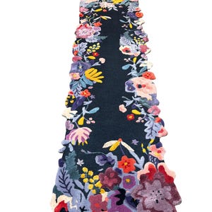 Puede incluir: Una alfombra de pasillo azul oscuro con un dise&ntilde;o floral. La alfombra presenta un campo central azul oscuro bordeado por una vibrante variedad de flores coloridas en tonos de rojo, amarillo, morado y rosa. Los bordes de la alfombra siguen el patr&oacute;n floral.