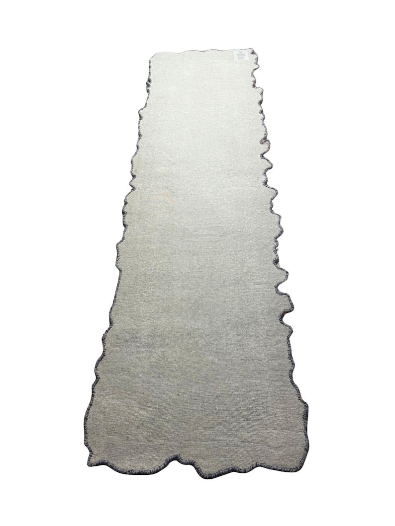 Puede incluir: Una alfombra rectangular gris claro con un borde &uacute;nico e irregular. La alfombra tiene una superficie texturizada y un borde gris oscuro que sigue la forma irregular. Dise&ntilde;ada para uso en interiores.