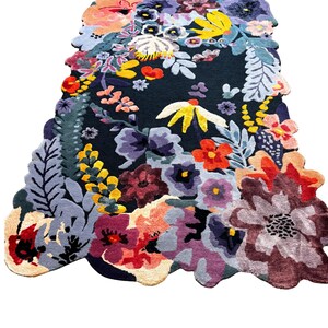 May include: A colourful floral rug featuring a dark background and a variety of flowers in shades of red, yellow, purple, and blue. The rug has an irregular shape and a textured appearance.