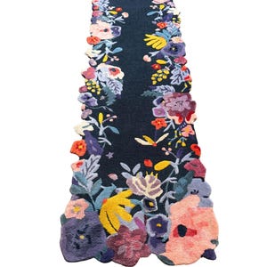 Puede incluir: Una alfombra de pasillo floral azul oscuro con una vibrante variedad de flores coloridas en tonos de rosa, morado, amarillo y naranja. Los bordes de la alfombra son festoneados y las flores est&aacute;n densamente empaquetadas a los lados.