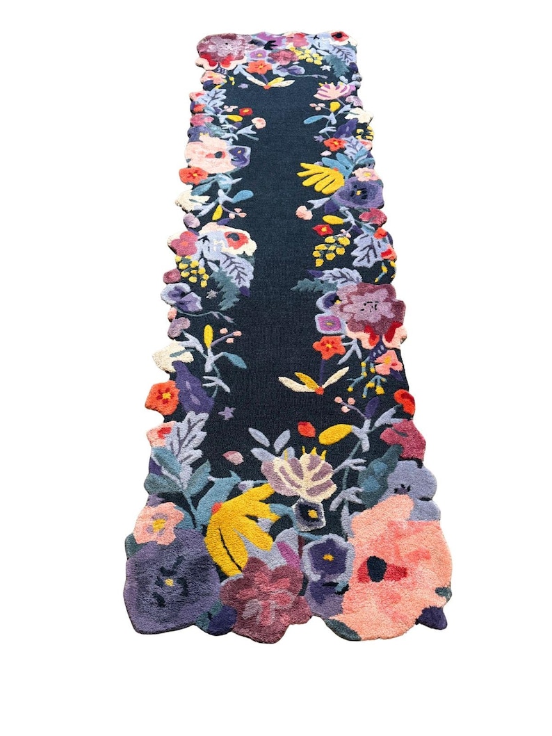 Puede incluir: Una alfombra de pasillo floral azul oscuro con una vibrante variedad de flores coloridas en tonos de rosa, morado, amarillo y naranja. Los bordes de la alfombra son festoneados y las flores est&aacute;n densamente empaquetadas a los lados.