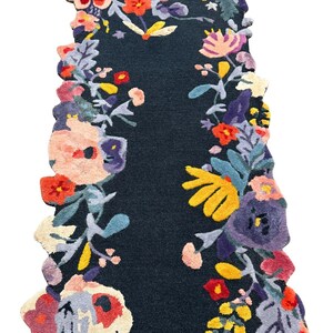 Puede incluir: Una alfombra de pasillo azul oscuro con un dise&ntilde;o floral. La alfombra presenta un campo central azul oscuro enmarcado por un borde de flores coloridas en tonos de rojo, amarillo, morado y rosa. Los bordes de la alfombra son festoneados.