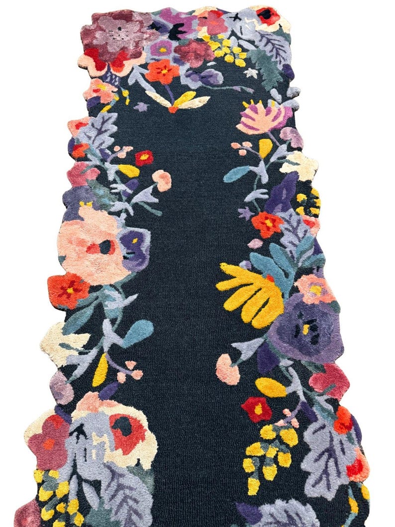Puede incluir: Una alfombra de pasillo azul oscuro con un dise&ntilde;o floral. La alfombra presenta un campo central azul oscuro enmarcado por un borde de flores coloridas en tonos de rojo, amarillo, morado y rosa. Los bordes de la alfombra son festoneados.