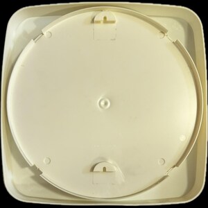 May include: A square, off-white plastic ceiling light fixture base with rounded corners. The center features a circular mounting plate with a central screw hole and two semi-circular locking tabs positioned at the top and bottom for secure installation.