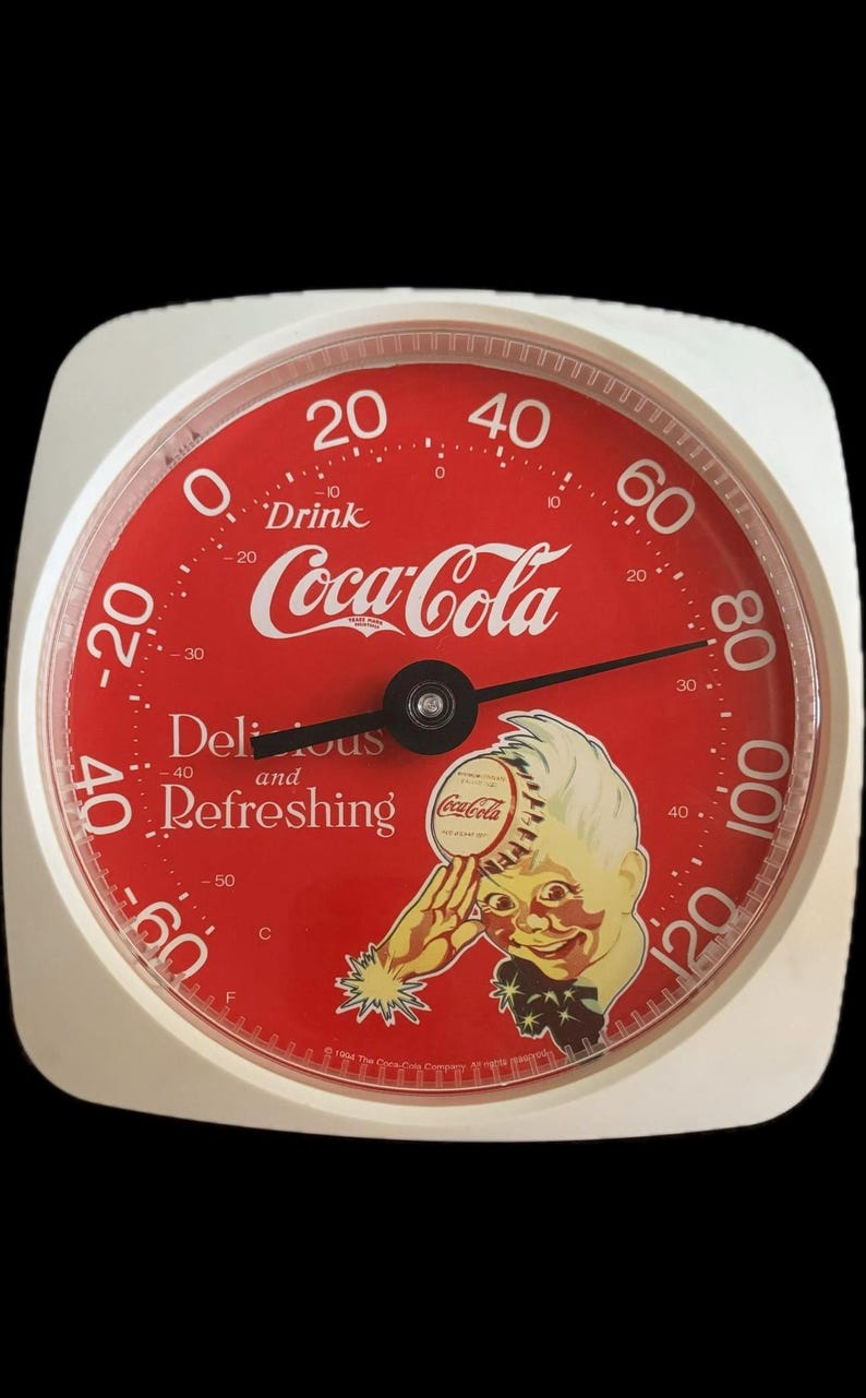 May include: A round Coca-Cola thermometer with a white frame and a red face. The dial features the text Drink Coca-Cola, Delicious and Refreshing, and a graphic of a person holding a bottle cap. It displays temperatures from -60 to 120 degrees Fahrenheit.