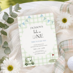 May include: A rectangular invitation card featuring a light green and white checkered pattern with blue bunting flags. The text reads Jackson's hole in ONE, TIME TO PAR-TEE!, and includes party details. Graphics include a golf cart and a golf flag.