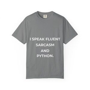 May include: A gray t-shirt with the text "I SPEAK FLUENT SARCASM AND PYTHON" in white. The shirt is a basic crew neck style, suitable for casual wear.