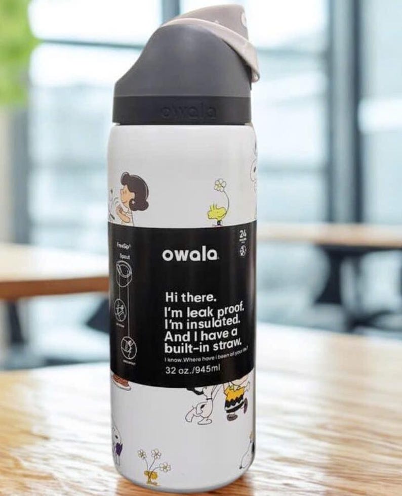 May include: A white Owala water bottle with a black lid and a built-in straw. The bottle features cartoon character illustrations and text that reads "Hi there. I'm leak proof. I'm insulated. And I have a built-in straw." It holds 32 oz.