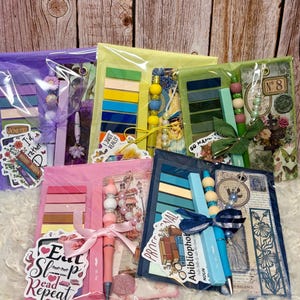 May include: Five stationery sets in clear plastic packaging, each containing a beaded pen, a stack of colorful sticky notes, a bookmark, and a themed sticker. The sets feature various color palettes including purple, yellow, green, pink, and blue.
