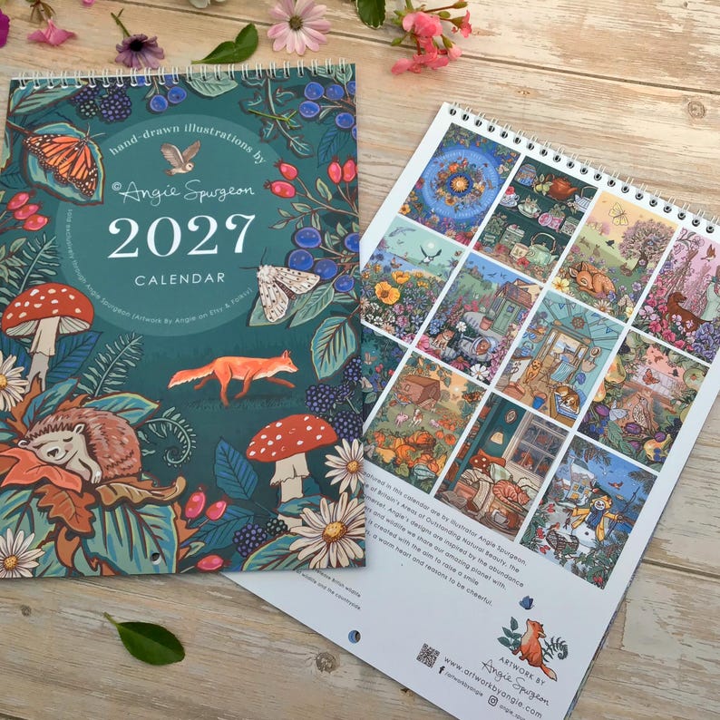 May include: A 2027 wall calendar with a dark teal cover featuring hand-drawn illustrations of a fox, hedgehog, mushrooms, and butterflies. The text reads 2027 CALENDAR and Angie Spurgeon. The back page displays a grid of twelve colorful nature scenes.