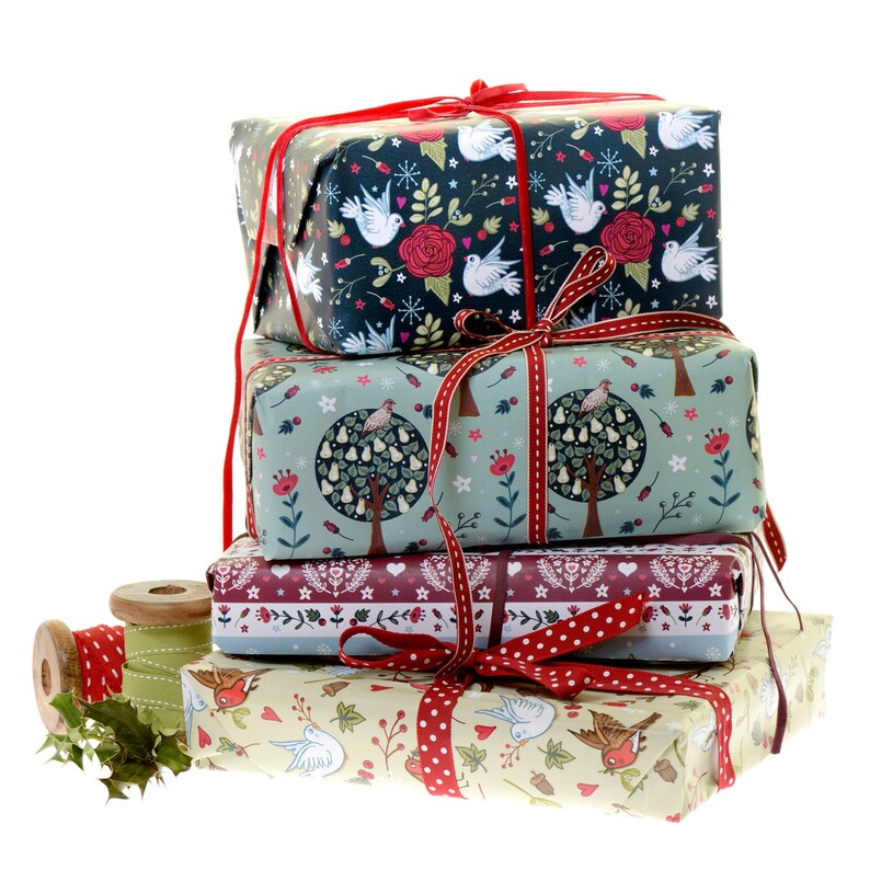 May include: A stack of five wrapped gifts with festive, colorful designs. The top gift is navy blue with white birds and red flowers. The second gift is green with a pear tree and red flowers. The third gift is burgundy with a white and red polka dot pattern. The fourth gift is cream with red birds and brown leaves. The bottom gift is wrapped in brown paper with a red ribbon.