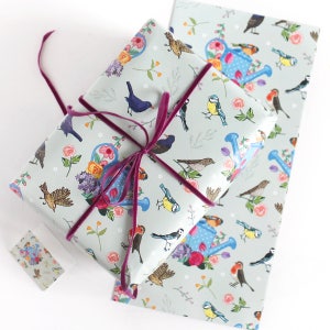Pu&ograve; includere: Carta da regalo a motivi blu e bianchi con un designo ripetitivo di uccelli, fiori e annaffiatoi. La carta &egrave; legata con un nastro viola.