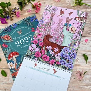 May include: A 2027 wall calendar featuring hand-drawn illustrations by Angie Spurgeon. The cover displays a dark teal background with a butterfly, mushroom, and berries. The open page shows a person in a hat with a dog in a field of flowers.
