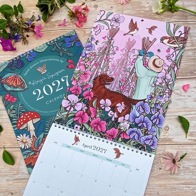 May include: A 2027 wall calendar featuring hand-drawn illustrations by Angie Spurgeon. The cover displays a dark teal background with a butterfly, mushroom, and berries. The open page shows a person in a hat with a dog in a field of flowers.