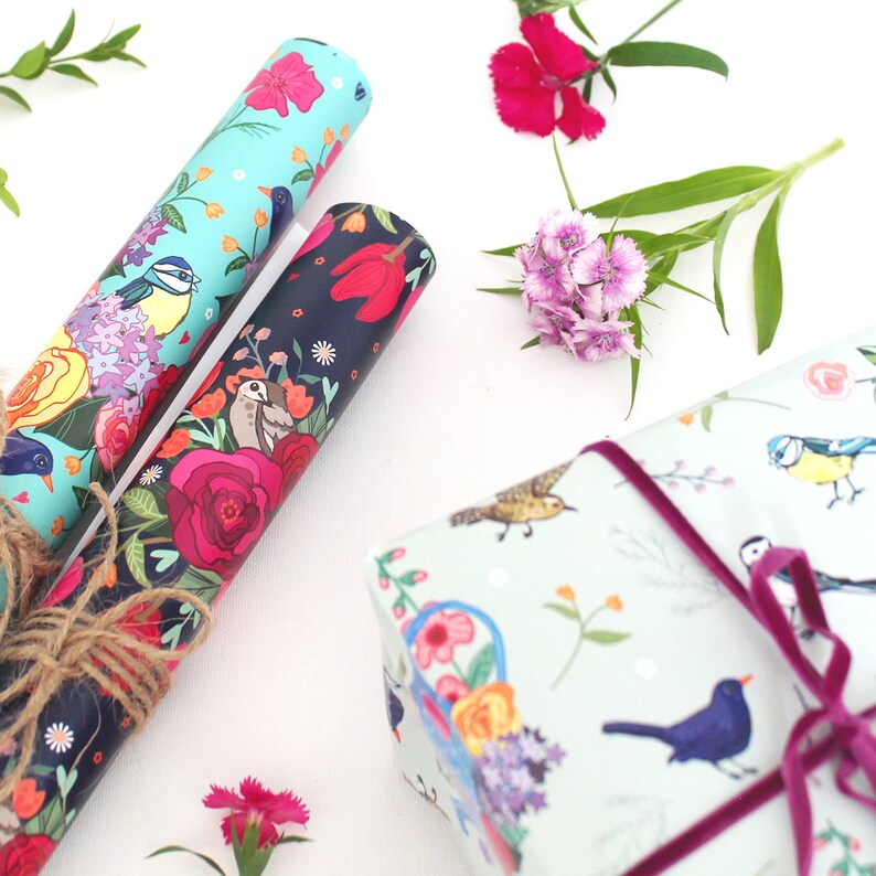 Pu&ograve; includere: Due rotoli di carta da regalo colorata con motivi floreali e di uccelli. Un rotolo &egrave; blu con uccelli e fiori bianchi, l'altro &egrave; nero con fiori rossi e uccelli marroni. Un terzo rotolo di carta da regalo &egrave; avvolto come una scatola regalo con un nastro rosa.