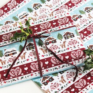 May include: A gift wrapped in blue and red patterned wrapping paper with a brown ribbon. The paper features a winter scene with houses, trees, and deer. The gift is topped with a sprig of holly.