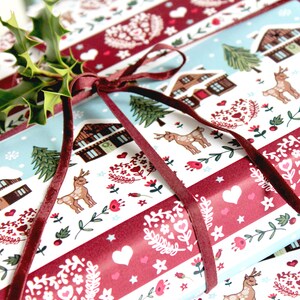 May include: Red and white striped wrapping paper with a winter scene featuring houses, trees, deer, and hearts. The paper is tied with a burgundy velvet ribbon.
