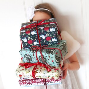 May include: A stack of four wrapped gifts with festive holiday designs. The gifts are wrapped in paper with birds, trees, and floral patterns. The top gift is wrapped in dark blue paper with white birds and red flowers. The second gift is wrapped in light blue paper with green trees and red flowers. The third gift is wrapped in cream paper with red and white polka dots and a floral pattern. The bottom gift is wrapped in red paper with a white and blue floral pattern.