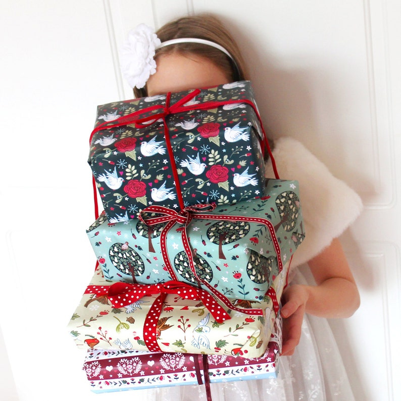 May include: A stack of four wrapped gifts with festive holiday designs. The gifts are wrapped in paper with birds, trees, and floral patterns. The top gift is wrapped in dark blue paper with white birds and red flowers. The second gift is wrapped in light blue paper with green trees and red flowers. The third gift is wrapped in cream paper with red and white polka dots and a floral pattern. The bottom gift is wrapped in red paper with a white and blue floral pattern.