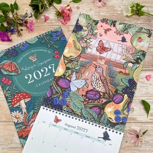 May include: Two 2027 wall calendars with spiral bindings featuring hand-drawn illustrations by Angie Spurgeon. The designs showcase vibrant botanical and wildlife scenes including mushrooms, butterflies, birds, berries, and a greenhouse interior.