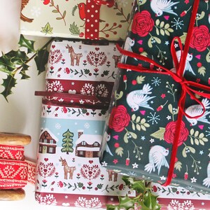May include: Three different Christmas wrapping paper designs. One is green with white doves and red roses, another is red and white with a winter village scene, and the third is green and white with a red and white polka dot ribbon.