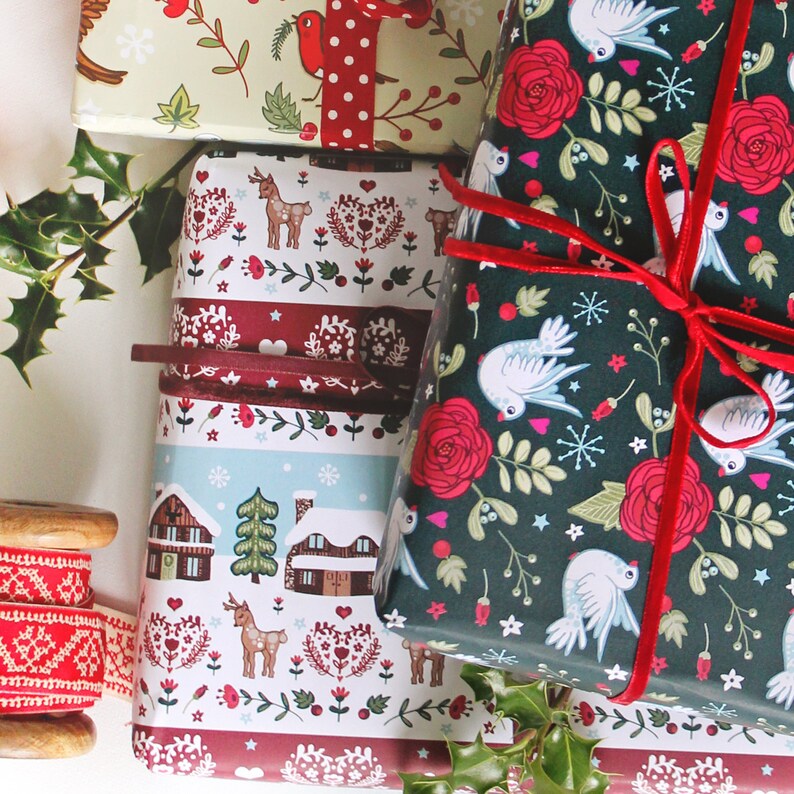 May include: Three different Christmas wrapping paper designs. One is green with white doves and red roses, another is red and white with a winter village scene, and the third is green and white with a red and white polka dot ribbon.