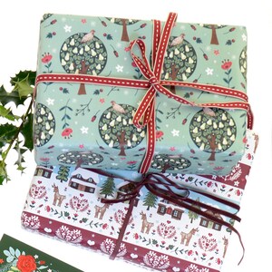 May include: Two wrapped gifts with festive Christmas paper. The top gift is wrapped in light blue paper with a pear tree design and a red ribbon. The bottom gift is wrapped in white paper with a red and white border and a brown ribbon. The paper features a winter scene with houses, trees, and deer.