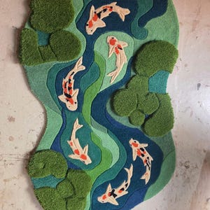 May include: A tufted rug featuring an irregular, organic shape with a pond scene. The design includes shades of green and blue water with several white, orange, and black koi fish swimming among clusters of textured green lily pads.