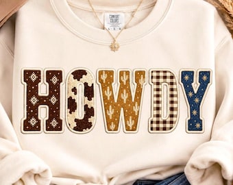 May include: A cream-colored crewneck sweatshirt featuring the word HOWDY in large block letters. Each letter has a unique pattern: brown geometric, cow print, mustard cactus, brown gingham, and navy blue with gold starbursts.