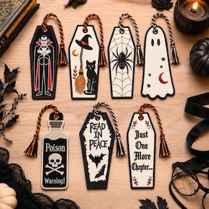 May include: Seven embroidered bookmarks featuring Halloween themes: a vampire, a cat with a broom, a spider web, a ghost, a poison bottle with a skull, a coffin with the text Read In Peace, and a coffin with the text Just One More Chapter.