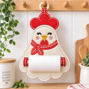 May include: A cream-colored felt paper towel holder shaped like a chicken with a red polka-dot comb, a yellow beak, and a red-and-white checkered scarf. The chicken features embroidered eyes and pink cheeks, holding a roll of white paper towels.