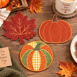 Puede incluir: Tres posavasos de tela con motivos otoñales: uno con forma de hoja de arce roja, otro con forma de calabaza naranja y un posavasos circular con un diseño de calabaza de patchwork en tonos naranja, amarillo y verde a cuadros.