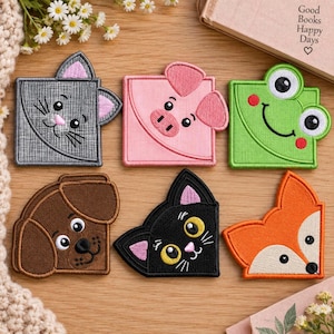 Puede incluir: Seis marcapáginas de esquina cuadrados con caras de animales bordadas: un gato gris, un cerdo rosa, una rana verde, un perro marrón, un gato negro y un zorro naranja. Cada marcapáginas está diseñado para deslizarse en la esquina de una página.