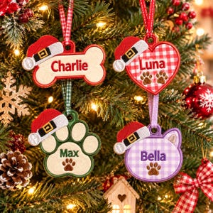 May include: Four embroidered Christmas ornaments shaped like a bone, heart, paw print, and cat head. Each features a red Santa hat, a hanging ribbon, and a name: Charlie, Luna, Max, or Bella. The heart and cat head have gingham patterns.