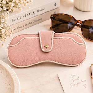 Peut inclure: Un étui à lunettes texturé rose poudré avec une silhouette incurvée, un passepoil blanc et une fermeture à bouton-pression dorée centrale. L'étui présente un design à rabat structuré et une finition mate lisse pour une protection optimale.