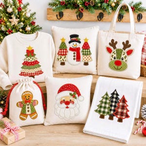 May include: A collection of cream-colored textile items featuring Christmas-themed embroidery, including a sweatshirt with a tree, two square pillows with a snowman and Santa, a tote bag with a reindeer, a drawstring pouch with a gingerbread man, and a towel with three trees.