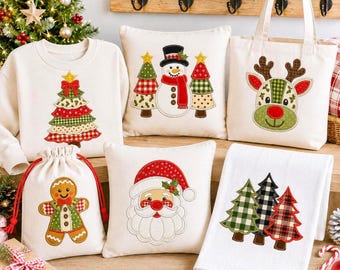May include: A collection of cream-colored textile items featuring Christmas-themed embroidery, including a sweatshirt with a tree, two square pillows with a snowman and Santa, a tote bag with a reindeer, a drawstring pouch with a gingerbread man, and a towel with three trees.