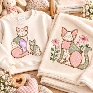May include: A cream-colored long-sleeve sweatshirt and a matching cream-colored blanket. The sweatshirt features an embroidered patch of a large cat and a kitten in patchwork patterns. The blanket features an embroidered cat with pink flowers.
