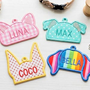May include: Embroidered pet tags in various shapes and colors. The tags include names like "LUNA", "MAX", "COCO", and "BELLA". The tags are in the shape of a dog's head, a crown, and a cat's head.