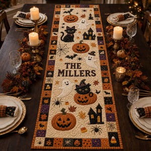 May include: A rectangular quilted table runner featuring a cream-coloured centre with Halloween motifs including pumpkins, black cats, ghosts, spiders, and haunted houses. The text THE MILLERS is printed in the centre. It has a multi-coloured border.