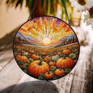 May include: A circular stained glass suncatcher featuring a vibrant sunset over a pumpkin patch. The design displays orange pumpkins in the foreground, rolling hills, and a bright sun radiating light across a multi-colored sky, all framed in black.