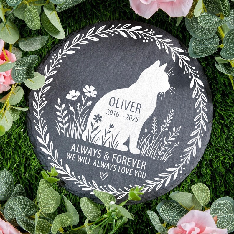 May include: A round, black slate pet memorial stone with a white cat silhouette, the name "Oliver" and dates 2016-2025. The text "ALWAYS & FOREVER WE WILL ALWAYS LOVE YOU" is below the cat. A white floral wreath surrounds the design.