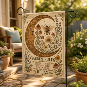 May include: A rectangular garden flag featuring a crescent moon with a human face, a bee, and various flowers in shades of brown, yellow, and green. The text reads: GARDEN RULES, LISTEN TO BIRDS, FEEL THE BREEZE, READ A BOOK, TAKE A NAP, SIP A DRINK, RELAX.