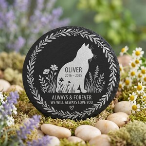 May include: A round, black slate memorial stone with a white cat silhouette, flowers, and foliage. The text reads "Oliver 2016-2025" and "Always & Forever We Will Always Love You." A decorative floral border surrounds the design.