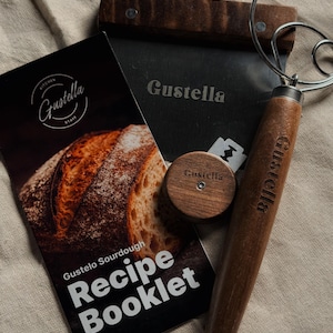 Peut inclure: Un kit de fabrication de pain au levain comprenant un livret de recettes Gustella, un fouet &agrave; p&acirc;te avec manche en bois fonc&eacute;, une corne de boulanger en m&eacute;tal avec manche en bois fonc&eacute; et une lame &agrave; pain ronde en bois, marqu&eacute;s du logo Gustella.