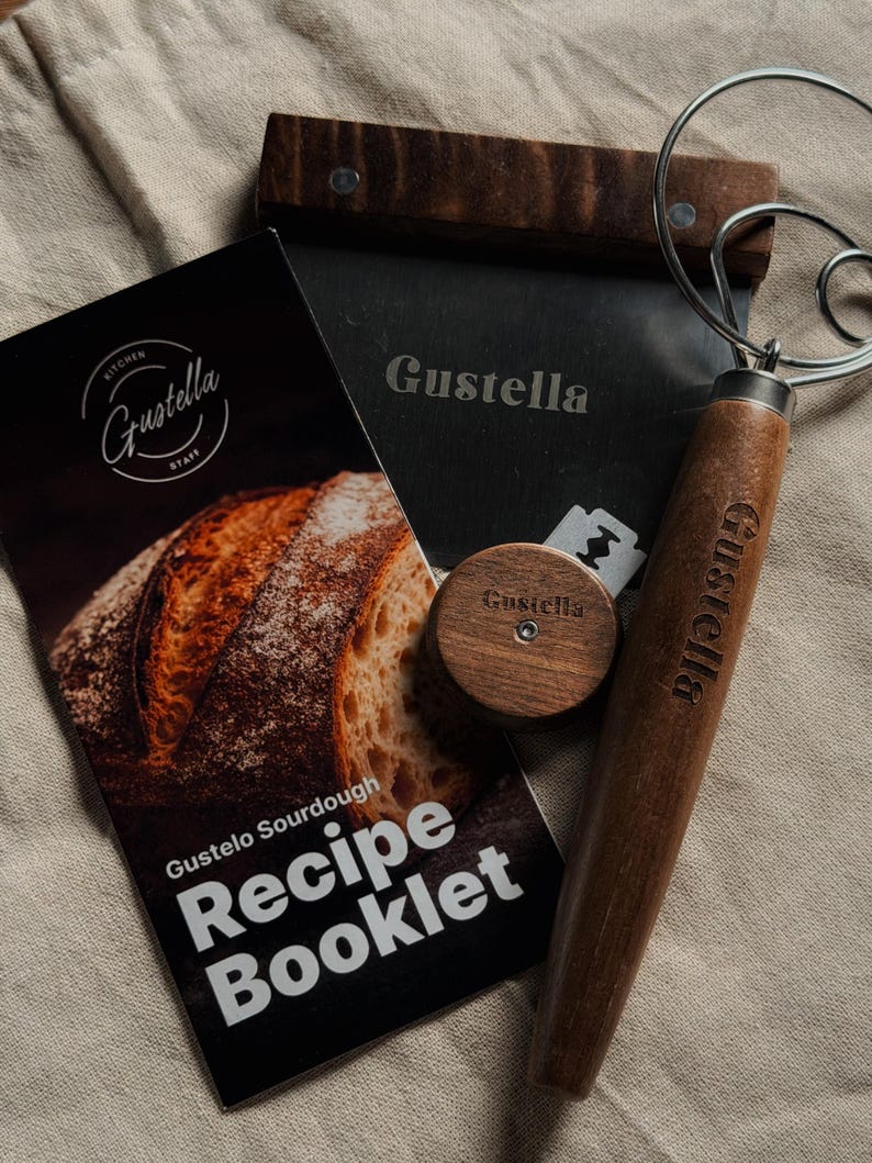 Peut inclure: Un kit de fabrication de pain au levain comprenant un livret de recettes Gustella, un fouet &agrave; p&acirc;te avec manche en bois fonc&eacute;, une corne de boulanger en m&eacute;tal avec manche en bois fonc&eacute; et une lame &agrave; pain ronde en bois, marqu&eacute;s du logo Gustella.