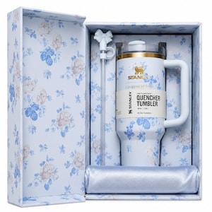 May include: A white Stanley Quencher tumbler with a floral design, presented in a matching gift box. The tumbler has a handle and a straw. The box and tumbler feature blue and white flowers. The tumbler holds 40 oz.