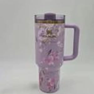 May include: A lavender insulated tumbler with a handle and a floral design. The tumbler has a clear lid and a matching lavender handle. The floral pattern includes pink and white flowers.