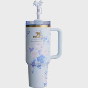 May include: A light blue Stanley Loveshack Fancy tumbler with a handle and a straw. The tumbler is decorated with a floral pattern in shades of blue and white. The top has a clear lid and a white bow on the straw.