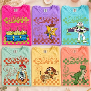 K&ouml;nnte beinhalten: Sechs kurz&auml;rmelige T-Shirts in Pink, Lila, Hellblau, Mint, Gelb und Orange. Jedes Shirt zeigt eine Toy Story-Charaktergrafik, darunter Aliens, Woody, Buzz Lightyear, Jessie, Slinky Dog und Rex, mit dem Text 1995 und einem Schachbrettmuster.
